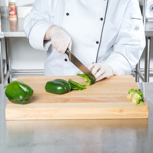 A person in a white coat cutting a green pepper on a Choice wood cutting board.