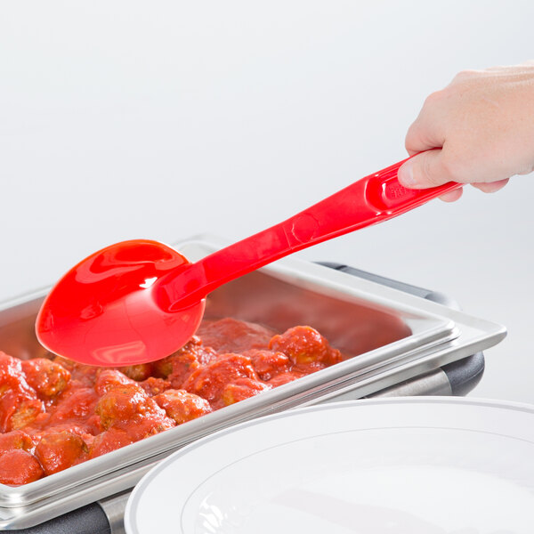 A person holding a red Cambro salad bar spoon over a tray of meatballs.