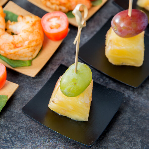 A Tablecraft black bamboo square dish filled with fruit and shrimp appetizers on a table.