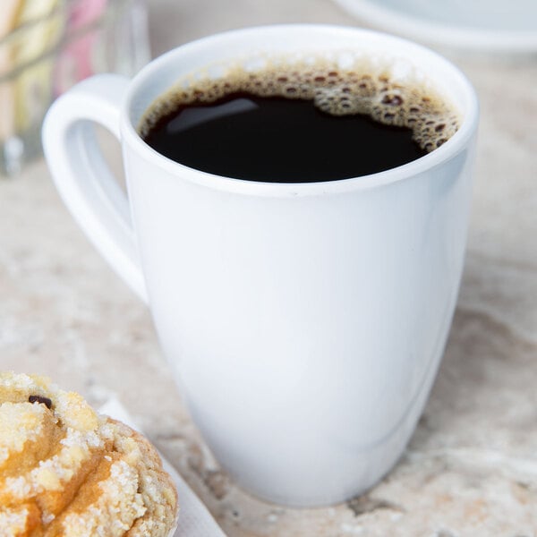 A white melamine mug filled with coffee on a table with a pastry.