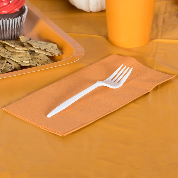 A Creative Converting pumpkin orange paper dinner napkin with a plastic fork on it.