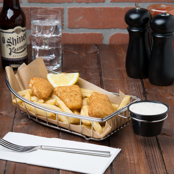 A Clipper Mill stainless steel boat basket filled with fried fish and fries on a table.