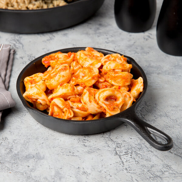 An Elite Global Solutions black faux cast iron fry pan filled with pasta and red sauce on a table.