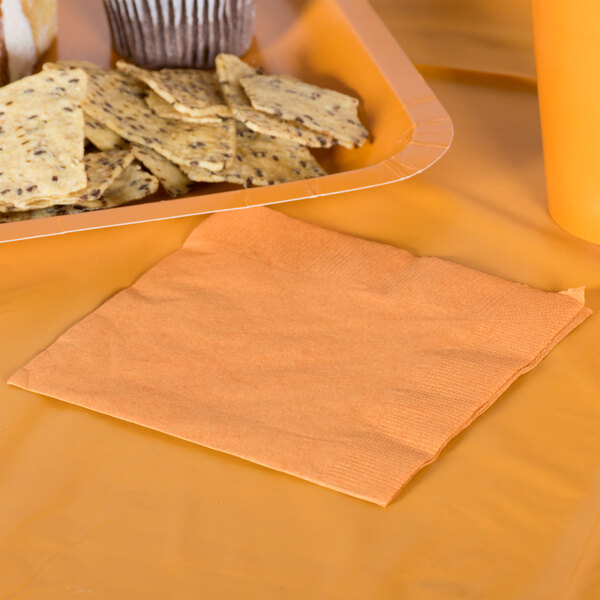 A Creative Converting Pumpkin Spice Orange beverage napkin on a table next to a plate of crackers.
