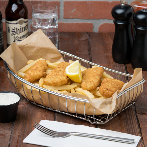 A Clipper Mill stainless steel boat basket filled with fish and chips on a table.