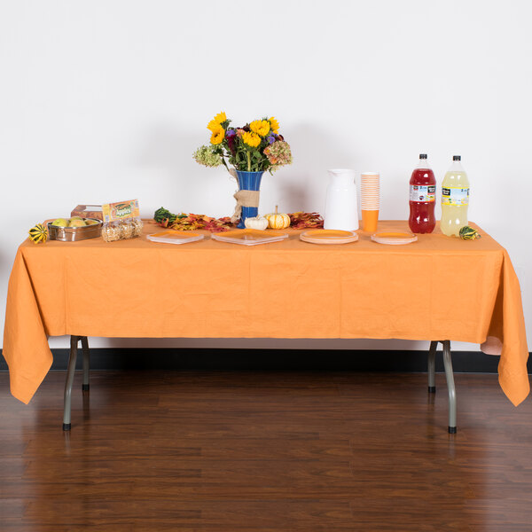 A table with a Creative Converting Pumpkin Spice Orange table cover and food on it.