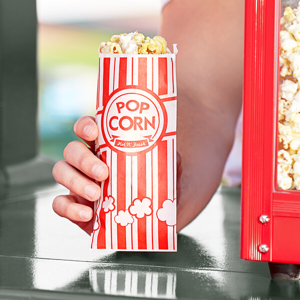 A hand holding a red and white striped Carnival King popcorn bag full of popcorn.