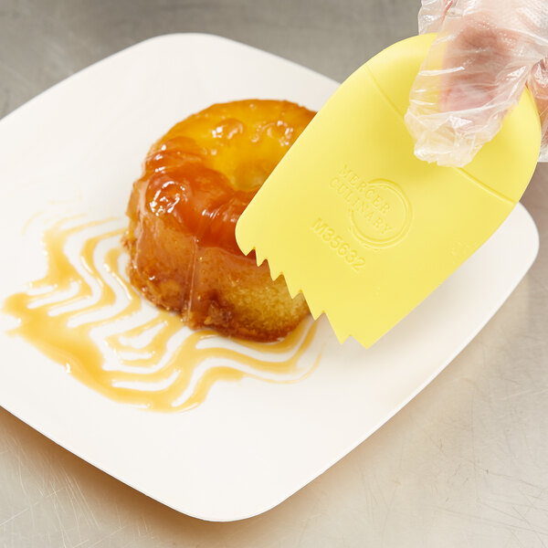 A hand using a Mercer Culinary saw tooth edge yellow silicone wedge to place a pastry on a plate.