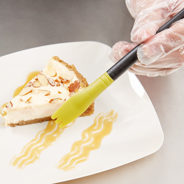 A person using a Mercer Culinary silicone brush to plate a slice of cheesecake.