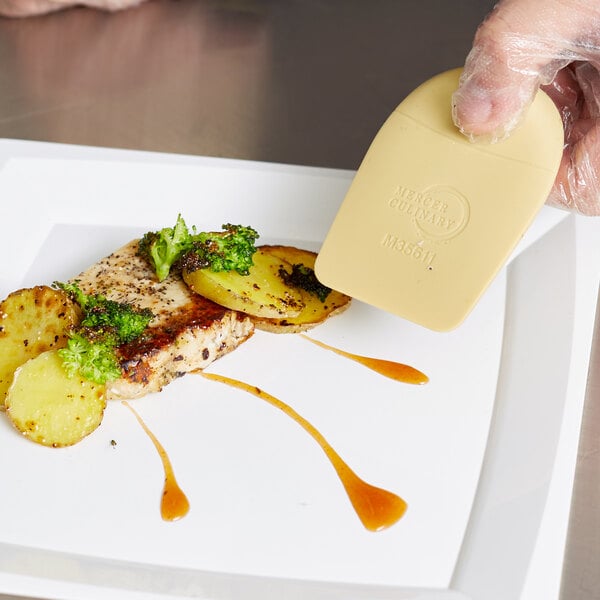 A person using a Mercer Culinary silicone wedge plating tool to place vegetables on a piece of meat.