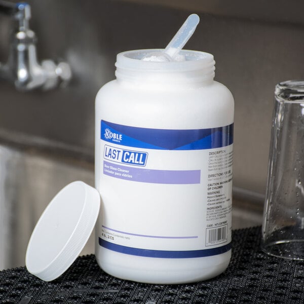 A white container of Noble Chemical Last Call Concentrated Powdered Bar Glass Cleaner with a white lid and a plastic spoon inside.