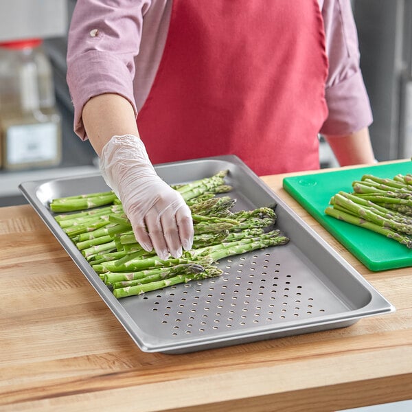 A person wearing gloves holding asparagus on a stainless steel tray.