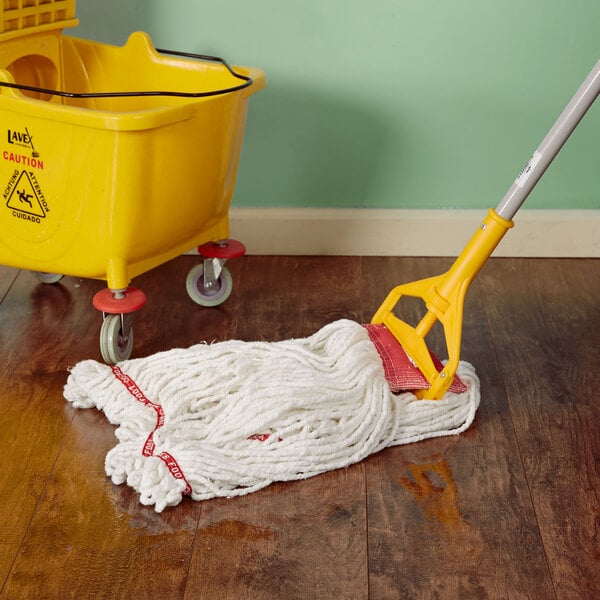A Rubbermaid white blend wet mop head with a yellow handle in a yellow bucket on a wood floor.