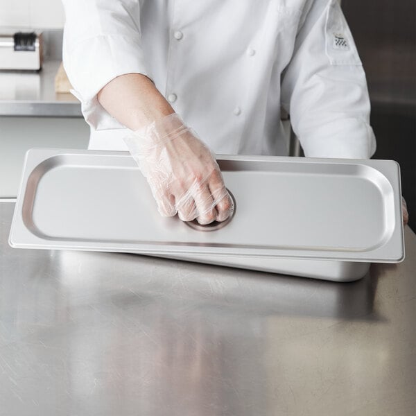 A person wearing plastic gloves places a Choice stainless steel steam table pan cover on a counter.