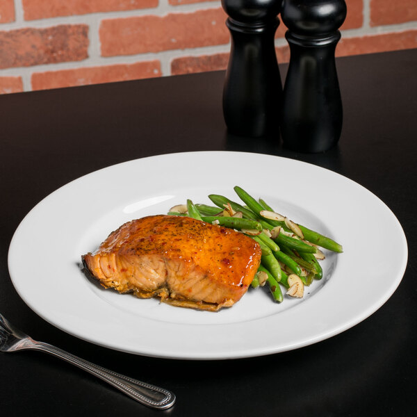 A Libbey Royal Rideau white porcelain plate with salmon and green beans on a table with a fork.