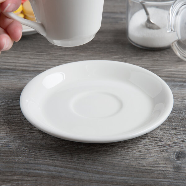 A hand pouring a white coffee cup into a white saucer.