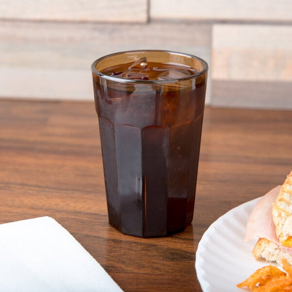 A Cambro amber plastic tumbler filled with brown liquid on a table next to a plate of food.