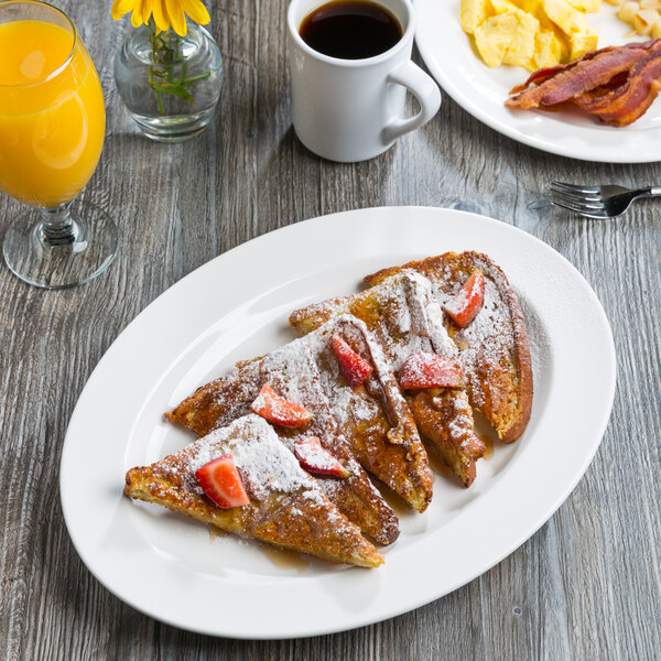 A Libbey white porcelain platter with french toast, bacon, and strawberries on a table.
