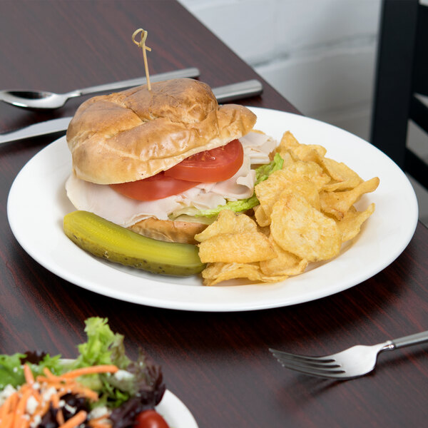 A Libbey round white porcelain plate with a sandwich and chips on it on a table.
