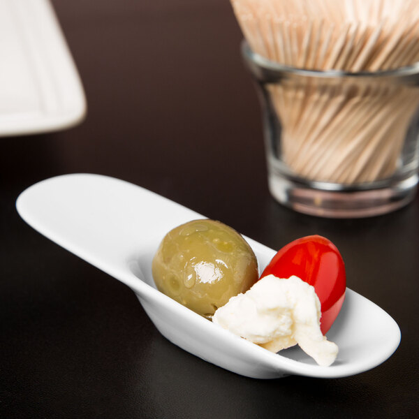 A Libbey white porcelain amuse bouche spoon on a white plate with a green olive and a white ball of cheese.