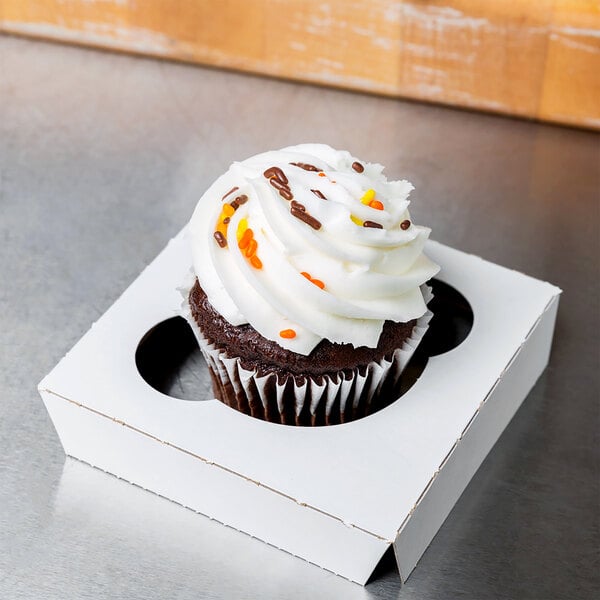 A Baker's Mark white box with a cupcake with white frosting and sprinkles inside.