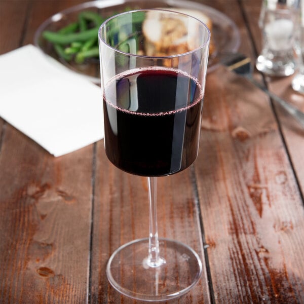 A clear plastic wine glass filled with red wine on a table.