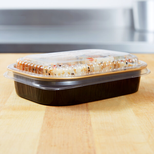 A Durable Packaging black and gold aluminum foil container with food inside on a table.