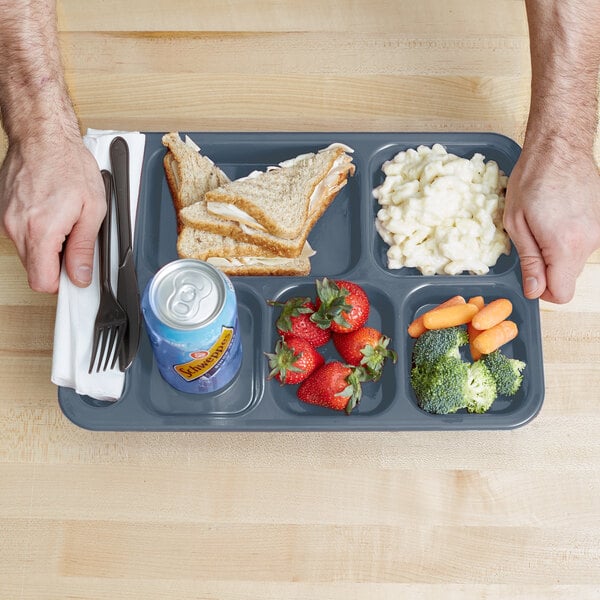 A Carlisle slate blue 6 compartment tray with a sandwich, fruit, and vegetables.