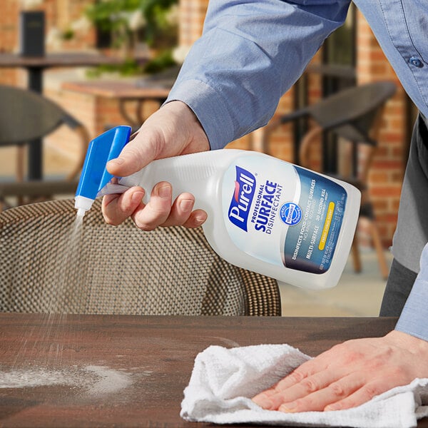 A person using Purell Fresh Citrus Professional Surface Disinfectant to clean a table outdoors with a spray bottle.