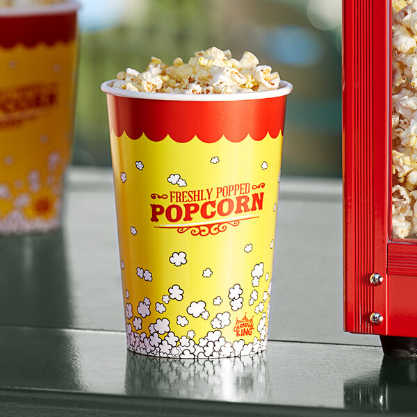A yellow and red Carnival King popcorn cup with white lid filled with popcorn.