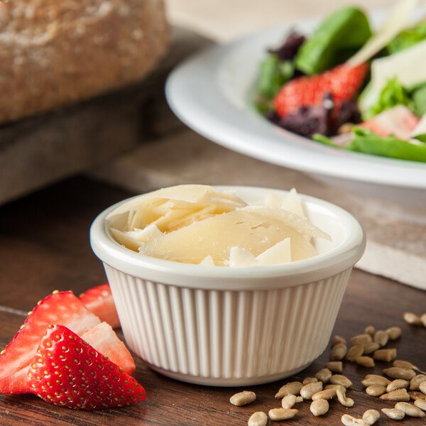 A bowl of cheese and fruit next to a salad in a fluted ramekin.