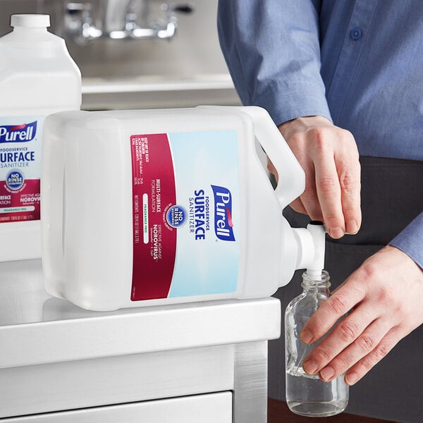 A person pouring Purell Foodservice Surface Sanitizer from a white jug with a red label.