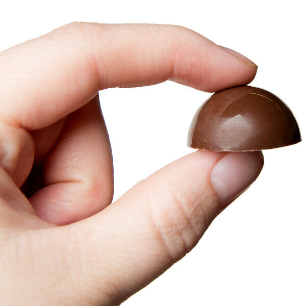 A hand holding a chocolate candy made with a Matfer Bourgeat half sphere candy mold.