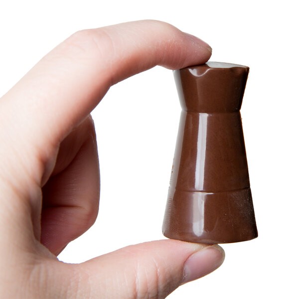 A hand holding a small brown Matfer Bourgeat chess piece made of chocolate.