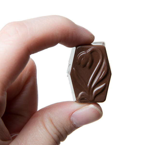 A hand holding a Matfer Bourgeat chocolate rectangle with a tulip design.