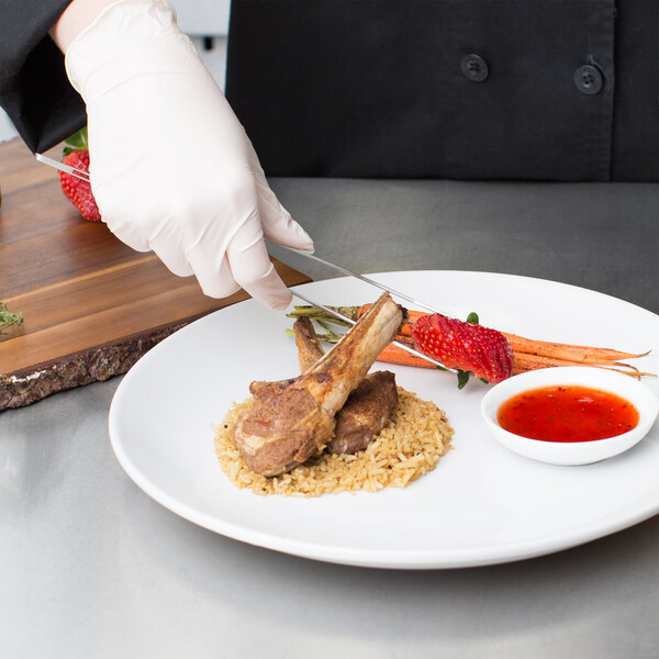 A person in a chef's uniform using Mercer Culinary plating tongs to cut meat on a plate.