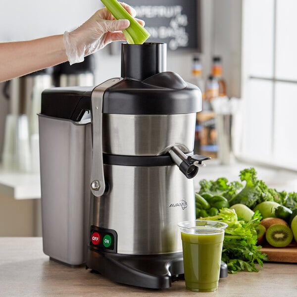 A hand putting celery into an AvaMix commercial juice extractor filled with green liquid.