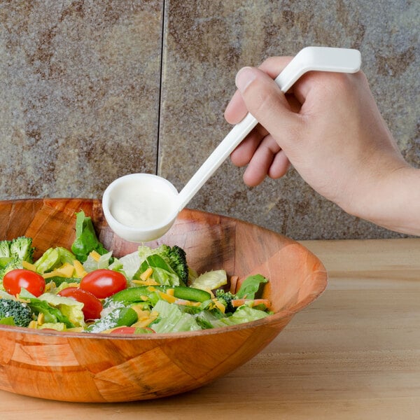 A hand holding a Cambro white plastic ladle over a white bowl of salad.