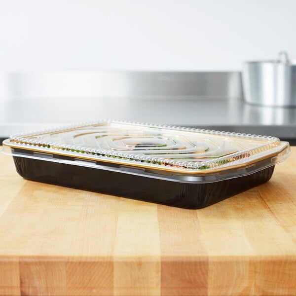 A Durable Packaging black and gold aluminum foil entree container with a dome lid on a counter.