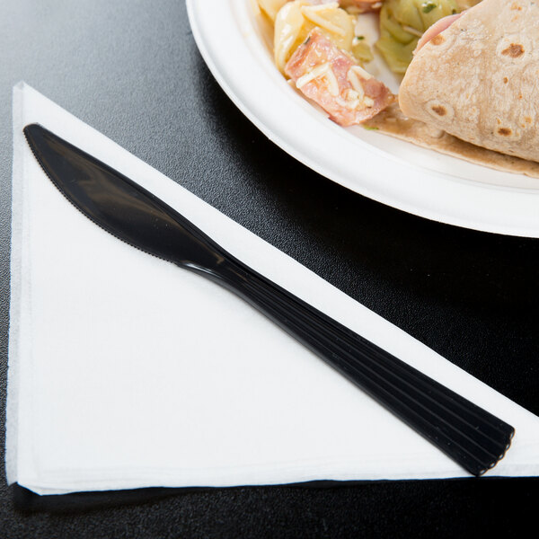 A black WNA Comet EcoSense plastic knife on a white plate with food.