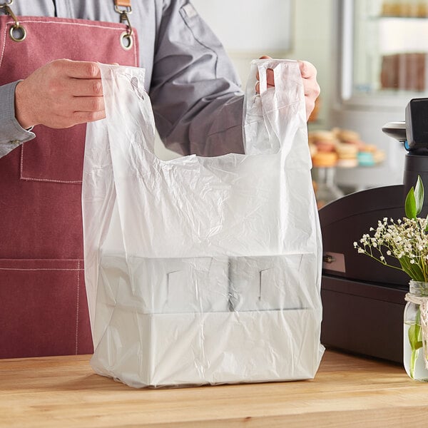 A man in an apron using a Choice clear plastic t-shirt bag to hold groceries on a counter in a deli.
