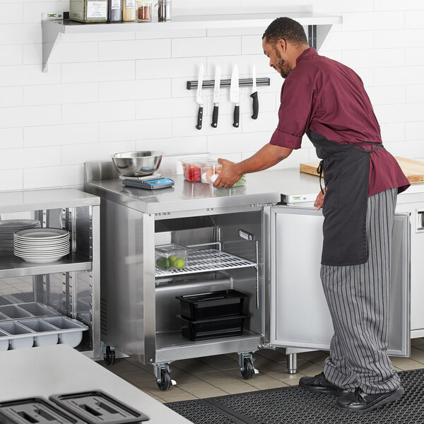 A man in a chef's uniform using an Avantco worktop freezer with a 3 1/2" backsplash in a professional kitchen.