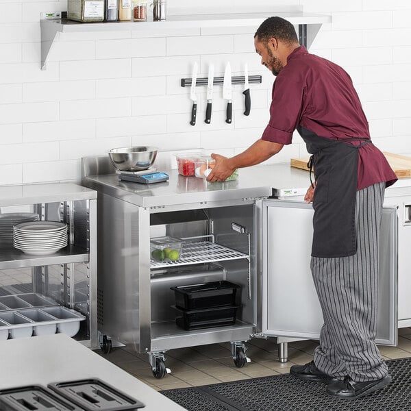 A man in a chef's uniform preparing food on a stainless steel worktop refrigerator.