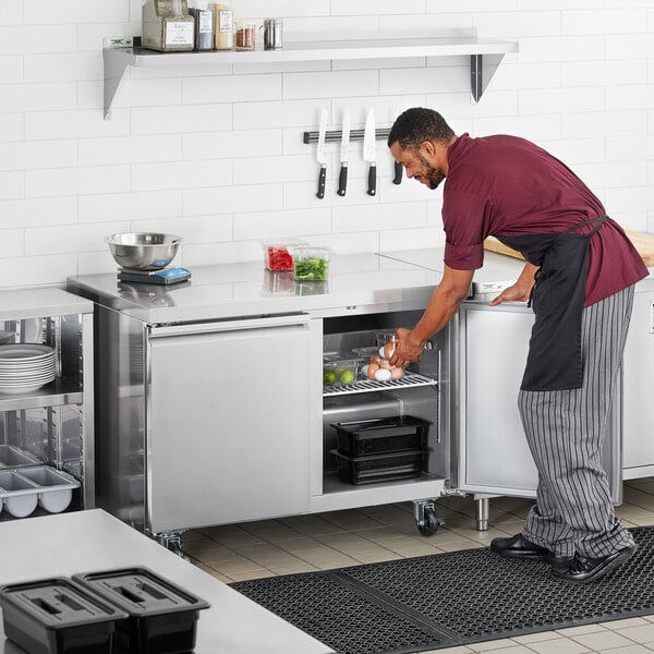 A man in a chef's uniform opening an Avantco undercounter refrigerator.