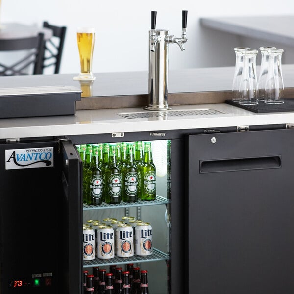 An Avantco black double tap kegerator with beer bottles and a tap.