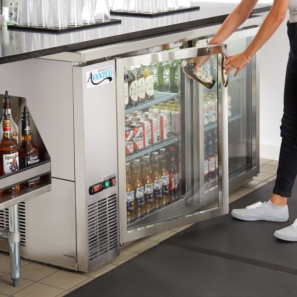 A woman opening an Avantco back bar refrigerator with bottles of beer.