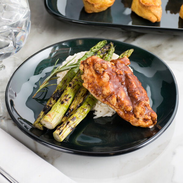 A GET green melamine coupe plate with chicken, asparagus, and rice on a marble table.