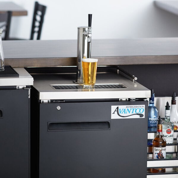 An Avantco black kegerator with a glass of beer on the counter.