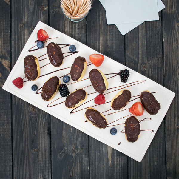 A white melamine display board with chocolate covered pastries and berries.
