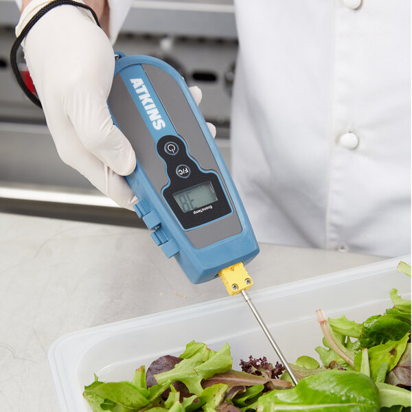 A hand holding a Cooper-Atkins EconoTemp thermocouple thermometer over a salad.